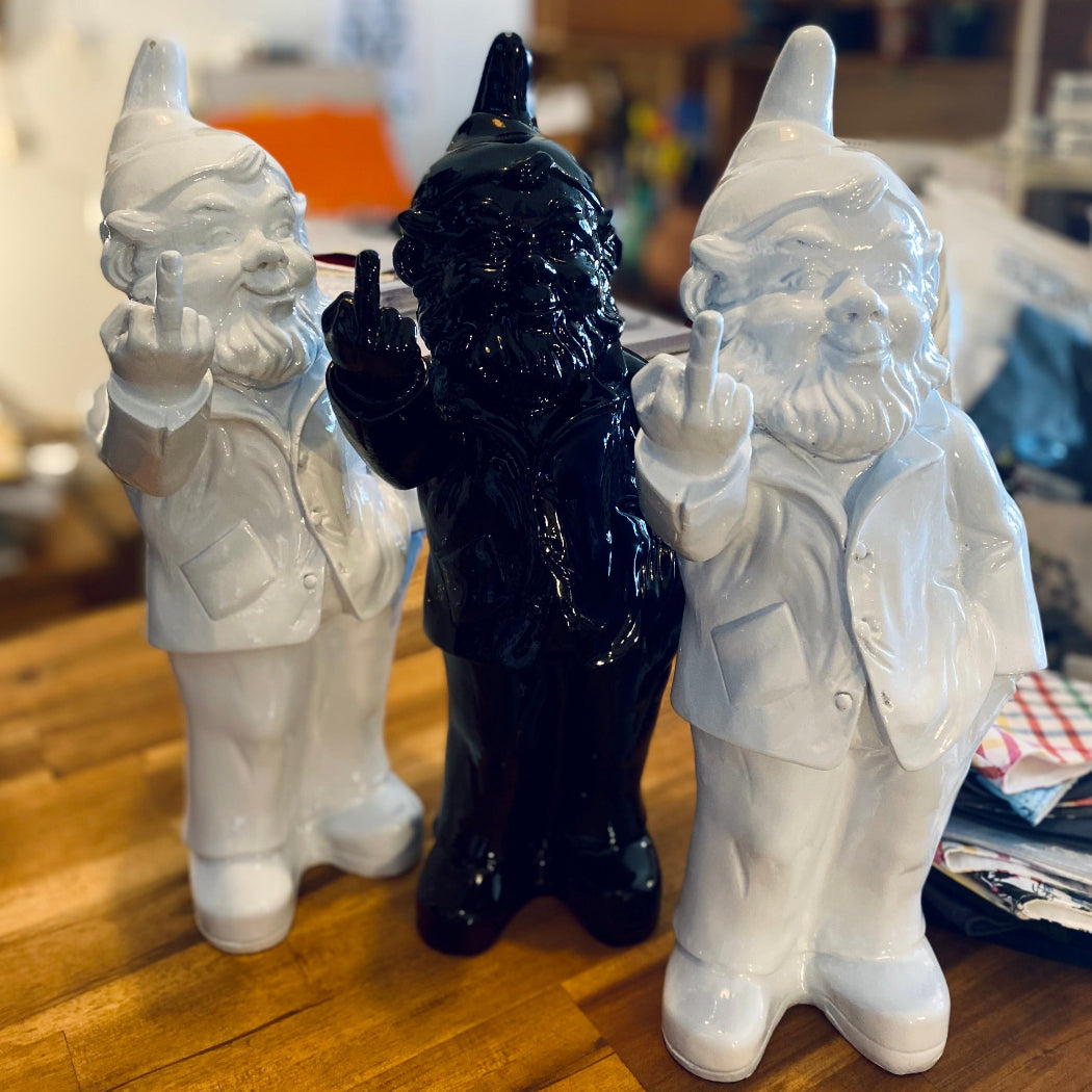 Two white gnomes and a black gnome figurine on a wooden surface.