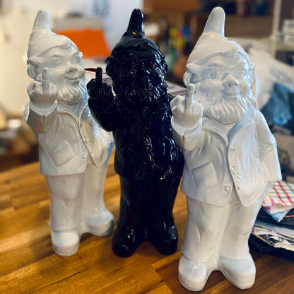 Two white gnomes and a black gnome figurine on a wooden surface.