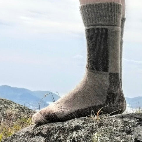 A person wearing brown boot socks standing on a rocky surface with hills in the background.