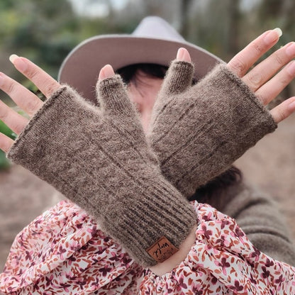 A person wearing brown fingerless mittens with a subtle cable knit pattern, holding hands up to show the mittens' length and fit.
