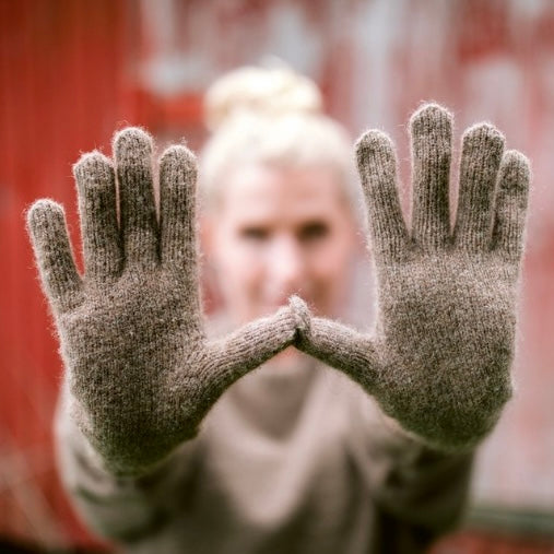 A person showing their hands wearing beige knitted gloves.